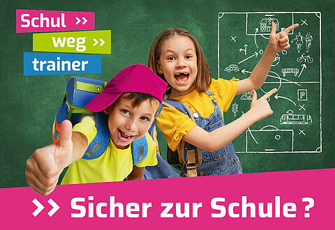 Zwei Schulkinder stehen vor einer Tafel und grinsen in die Kamera.