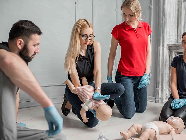 Zwei Frauen und zwei Männer üben an einer Babypuppe Erste-Hilfe-Maßnahmen.