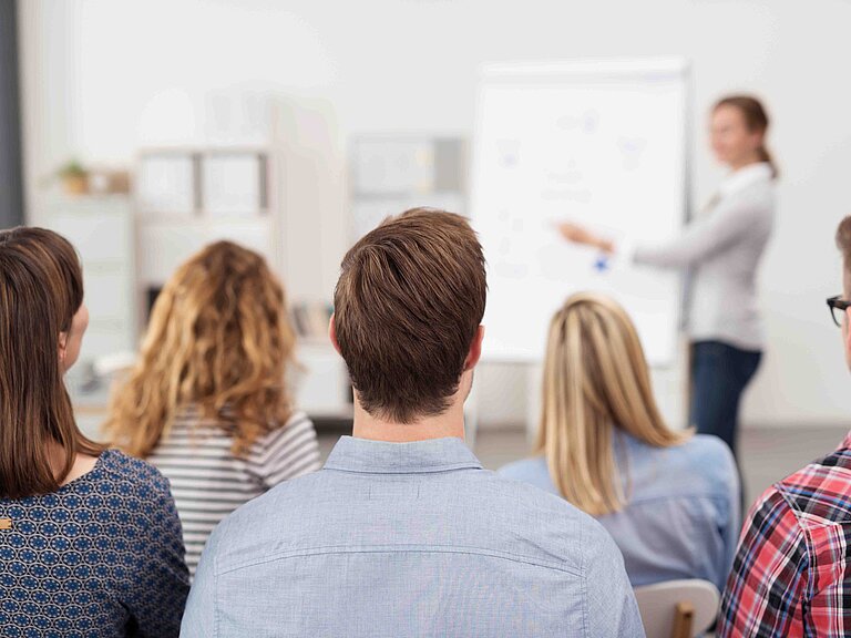 Mehrere Personen sitzen in einem Schulungsraum und hören einem Referenten zu.
