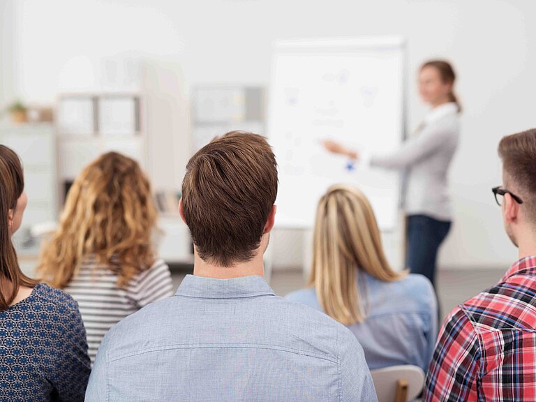 Mehrere Personen sitzen in einem Schulungsraum und hören einem Referenten zu.