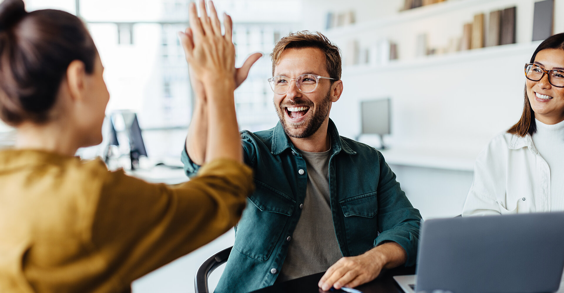 Ein junger Mann lächelt und schlägt zustimmend die Hände mit einer jungen Kollegin zusammen.