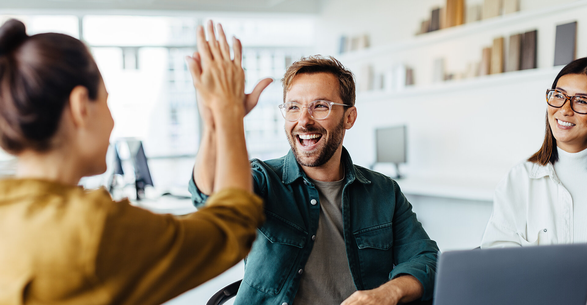 Ein junger Mann lächelt und schlägt zustimmend die Hände mit einer jungen Kollegin zusammen.
