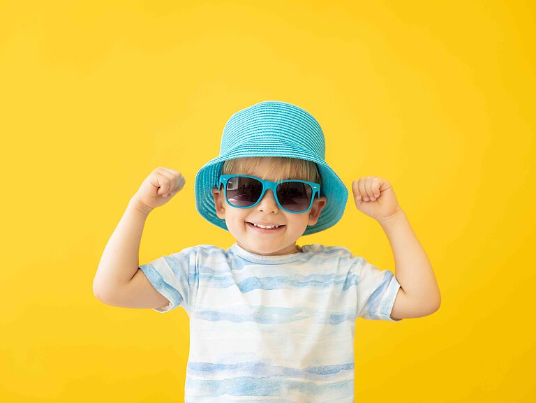 Ein Junge mit Sonnebrille trägt einen Sonnenhut auf dem Kopf.