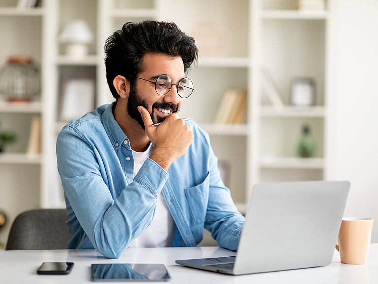Telecommuting Concept. Smiling Indian Man Working Online With Laptop At Home Office