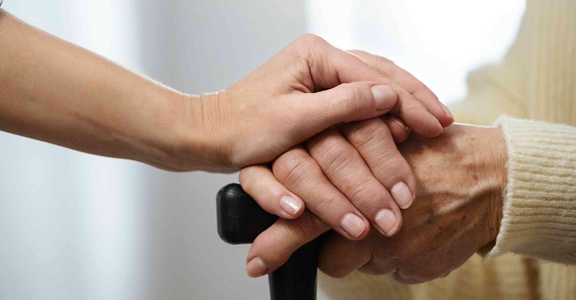 Zwei Händen greifen nacheinander. Es handelt sich um eine jüngere und eine ältere Hand mit Gehstock.