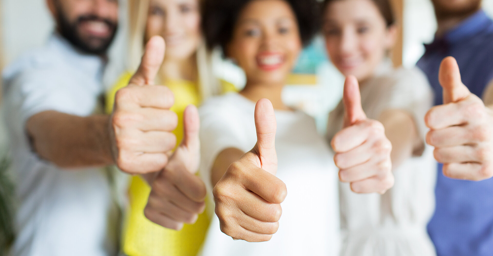 Mehrere Person lächeln in die Kamera und zeigen mit dem Daumen positiv nach oben