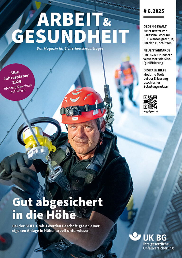 Titelbild Arbeit und Gesundheit. Mann hängt in persönlicher Schutzausrüstung von einer Decke und schaut in die Kamera. Portraitaufnahme.