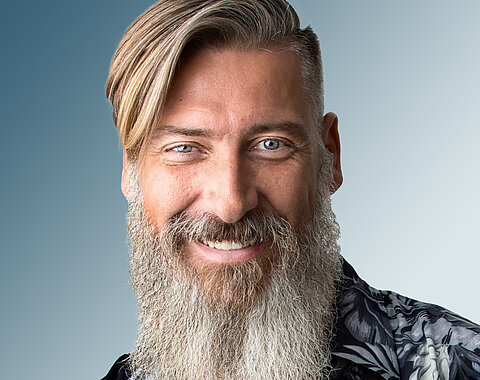 Ein Mann mit langem grauem Bart lächelt in die Kamera