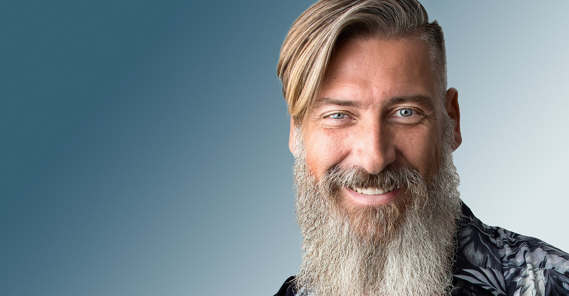 Ein Mann mit langem grauem Bart lächelt in die Kamera