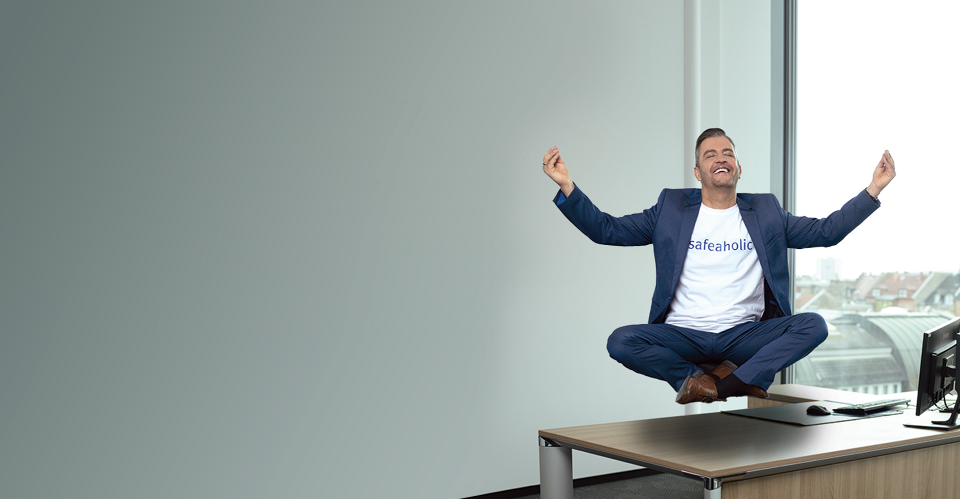 Ein Mann schwebt im Schneidersitz über einem Schreibtisch. Den Kopf hat er leicht nach oben geneigt, die Augen sind geschlossen und die Hände streckt er in die Höhe.