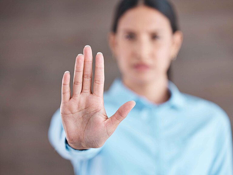 Frau schaut nach vorne und hebt die Rechte Hand schützend nach vorne.