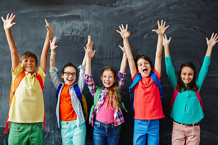 Schulkinder strecken vor der Tafel die Hände in die Luft