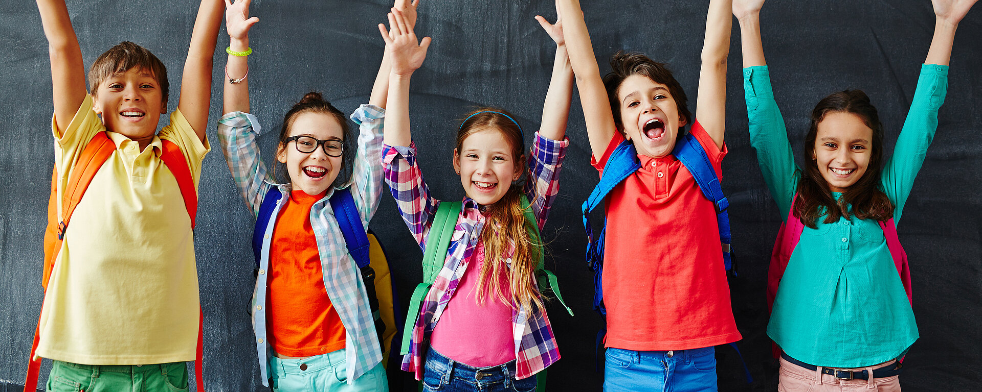 Schulkinder strecken vor der Tafel die Hände in die Luft