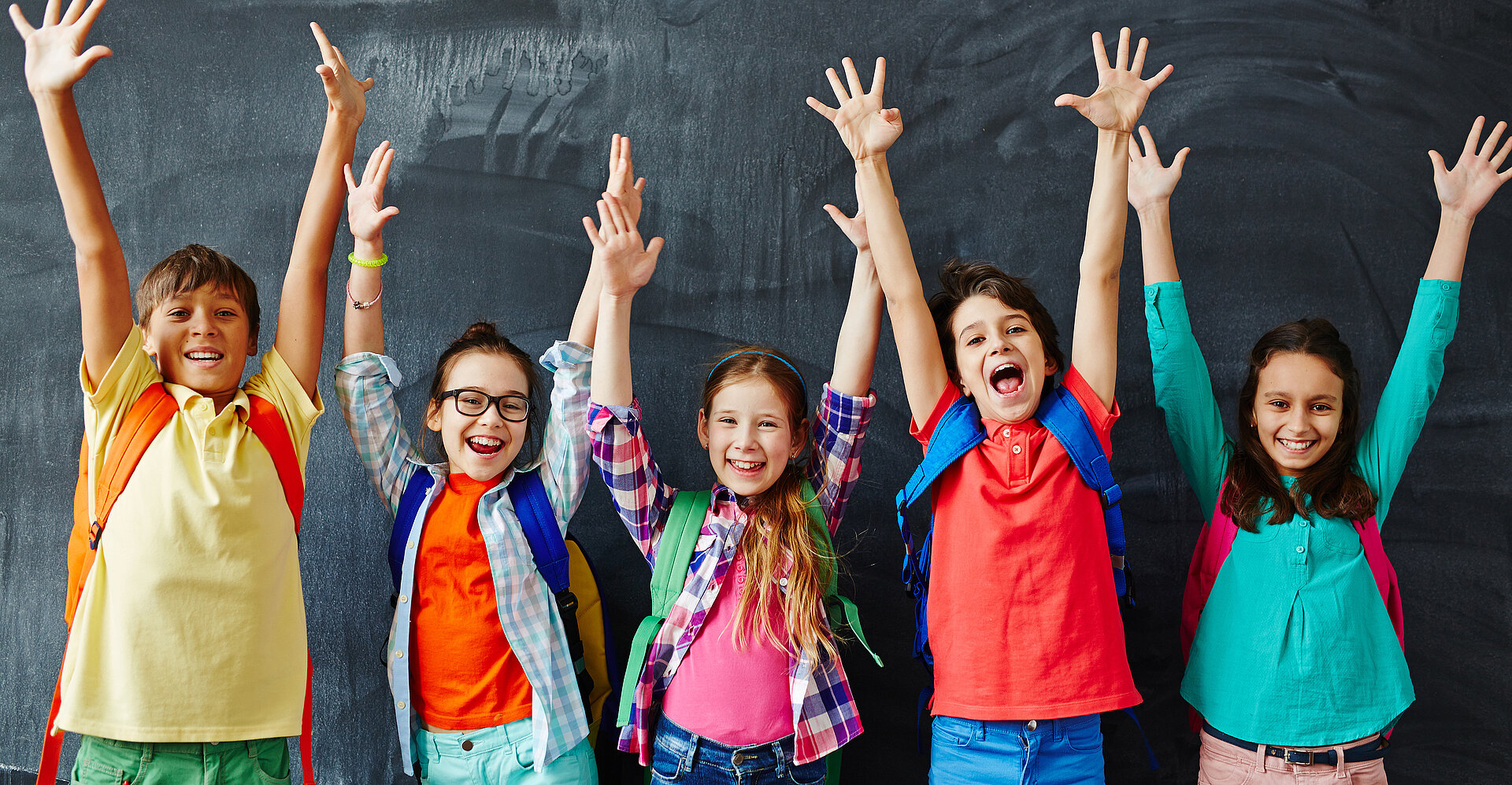 Schulkinder strecken vor der Tafel die Hände in die Luft