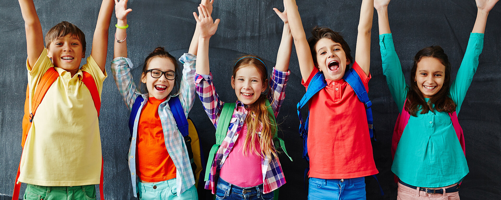 Schulkinder strecken vor der Tafel die Hände in die Luft
