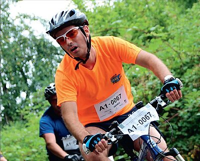 Ein Mann fährt Fahrrad. Dahinter sind noch zwei Personen auf Fahrrädern fahrend abgebildet.