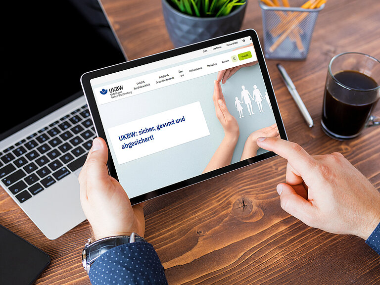 Hände streichen über ein Tablet. Auf dem Tablet ist die Startseite von www.ukbw.de zu sehen.