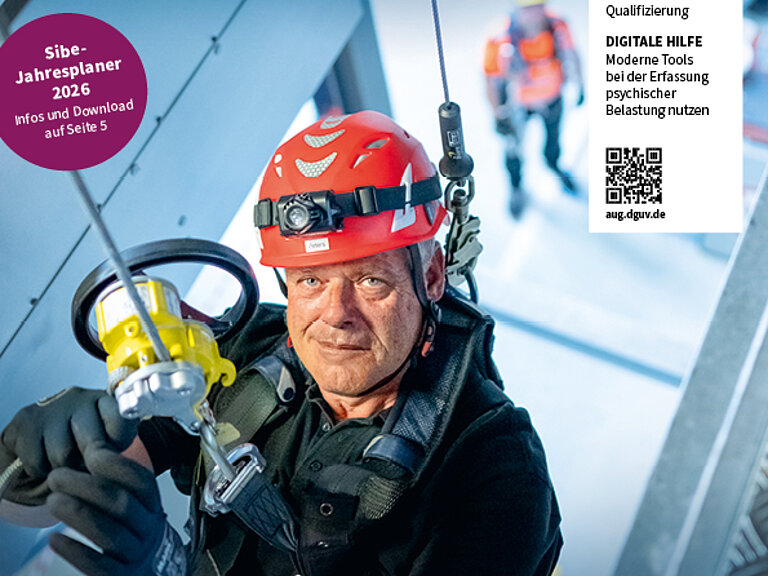 Titelbild Arbeit und Gesundheit. Mann hängt in persönlicher Schutzausrüstung von einer Decke und schaut in die Kamera. Portraitaufnahme.